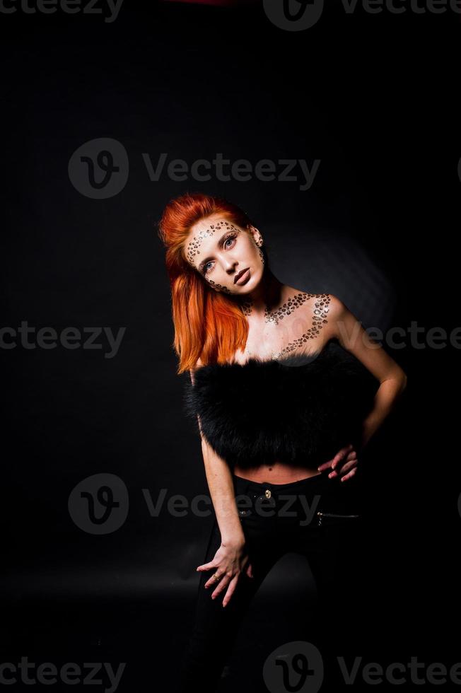 Fashion model red haired girl with originally make up like leopard predator isolated on black. Studio portrait. photo