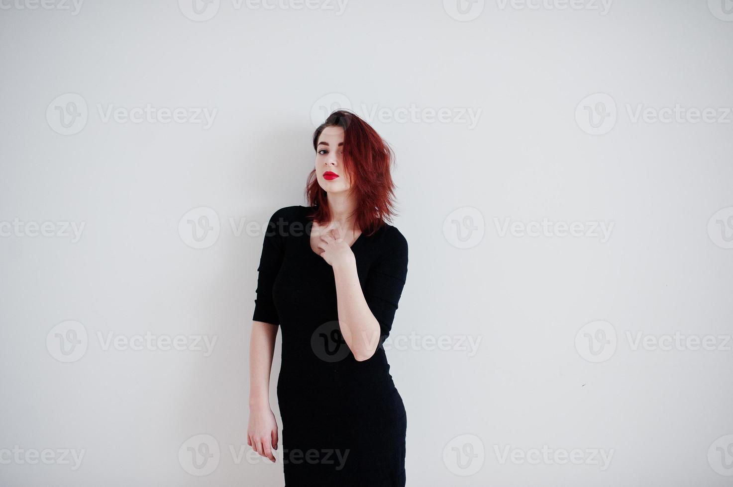chica pelirroja con túnica de vestido negro contra la pared blanca en la habitación vacía. foto