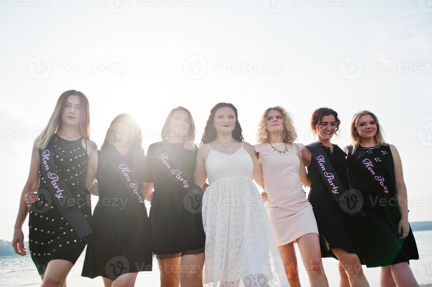 Group of 7 girls wear on black and 2 brides at hen party against sunny beach. photo