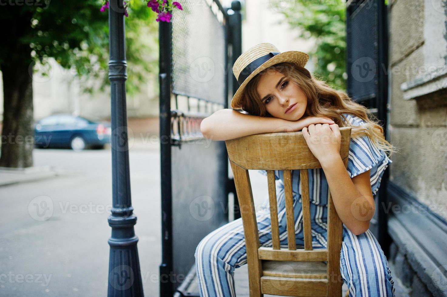 Portrait of a fabulous young woman in striped overall and hat sitting and posing on the chair outdoor. photo