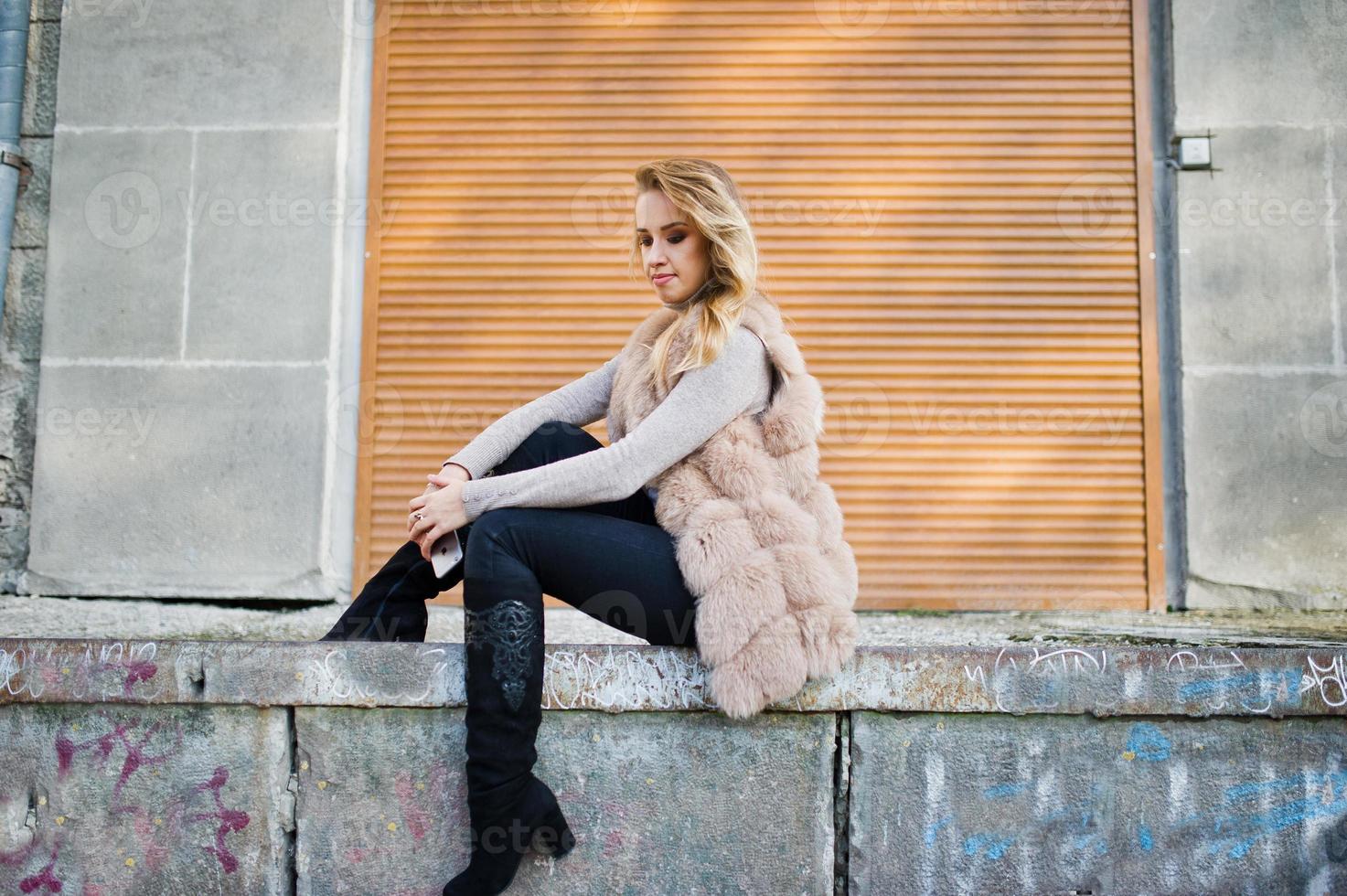 chica rubia en abrigo de piel contra la pared con persianas. foto