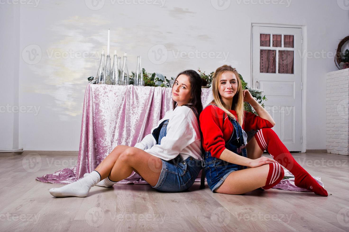 dos amigas hermosas y divertidas visten pantalones cortos de jeans y polainas contra la mesa con decoración de año nuevo. foto