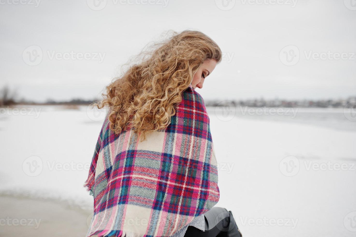 Curly blonde girl in checkered plaid against frozen lake at winter day. photo