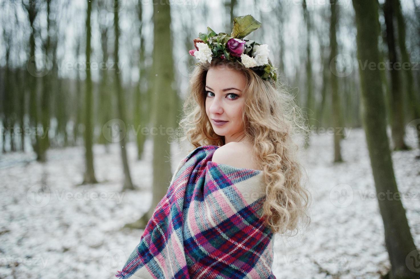 Curly cute blonde girl with wreath in checkered plaid at snowy forest in winter day. photo
