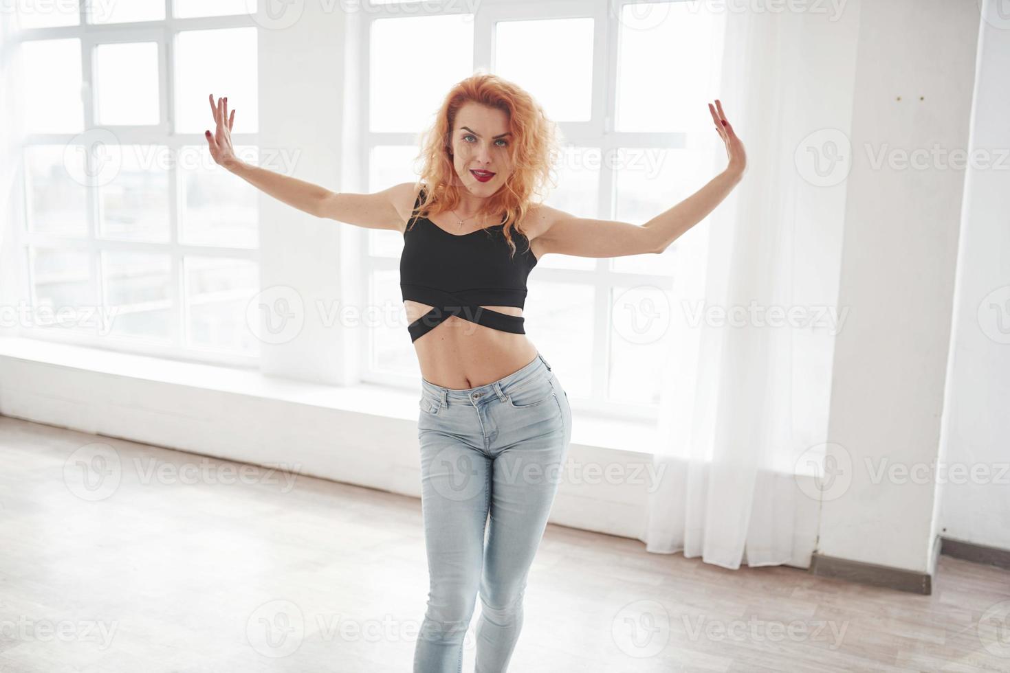 Hands to the sides. Attractive redhead woman posing in the spacey room near the window photo