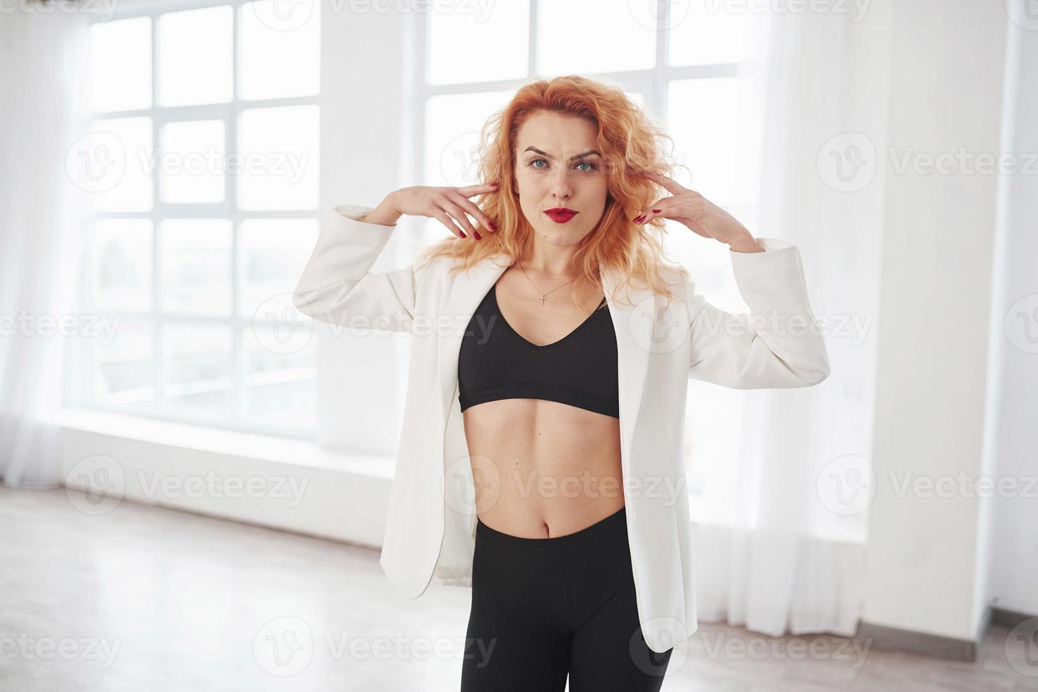 Gorgeous person. Attractive redhead woman posing in the spacey room near the window photo