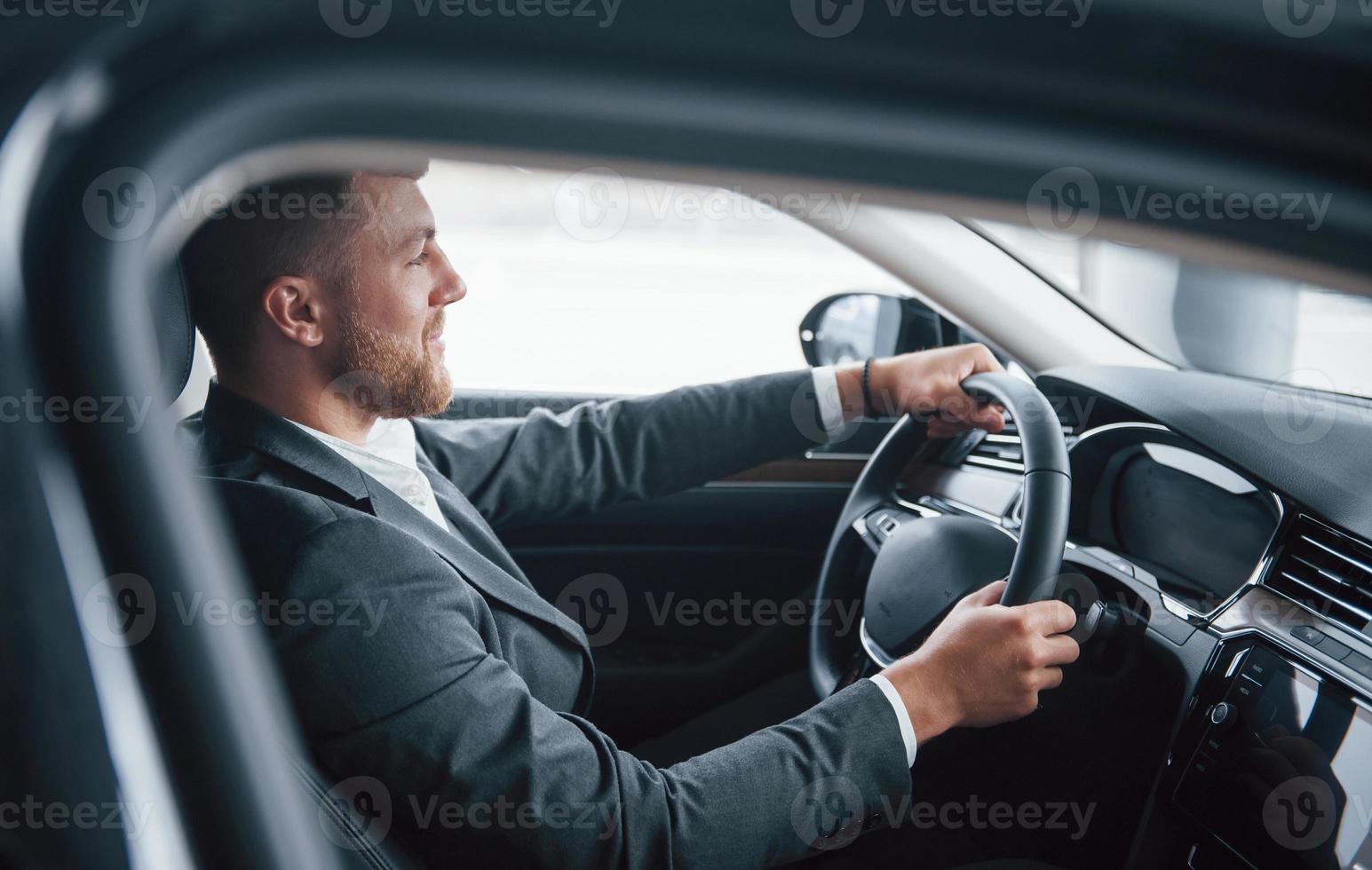 chico barbudo feliz. hombre de negocios moderno probando su auto nuevo en el salón del automóvil foto