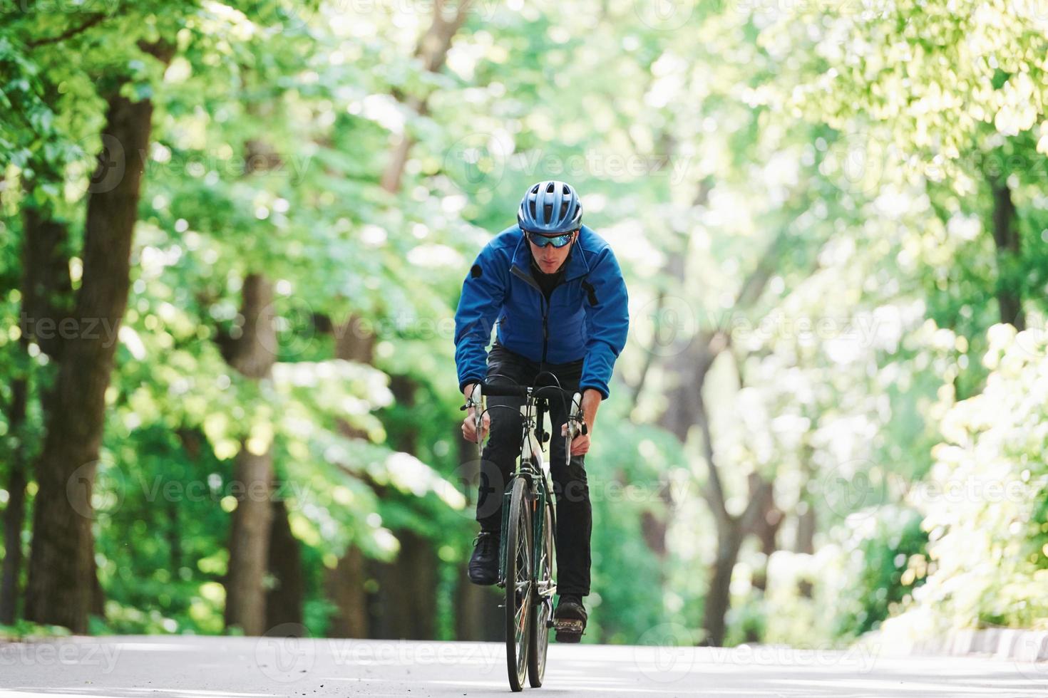 directo. ciclista en bicicleta está en la carretera asfaltada en el bosque en un día soleado foto