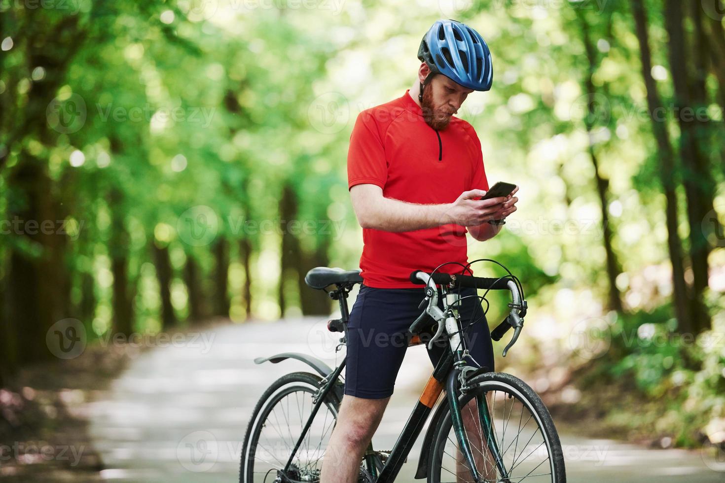 Chatting in internet. Cyclist on a bike is on the asphalt road in the forest at sunny day photo