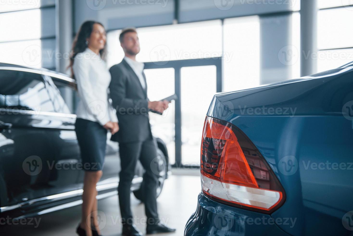 Rear of the blue painted car. Female customer and modern stylish bearded businessman in the automobile saloon photo