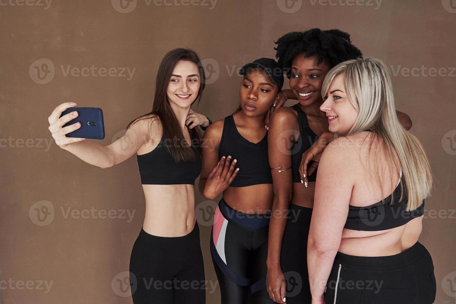 Let's take a picture. Group of multi ethnic women standing in the studio against brown background photo