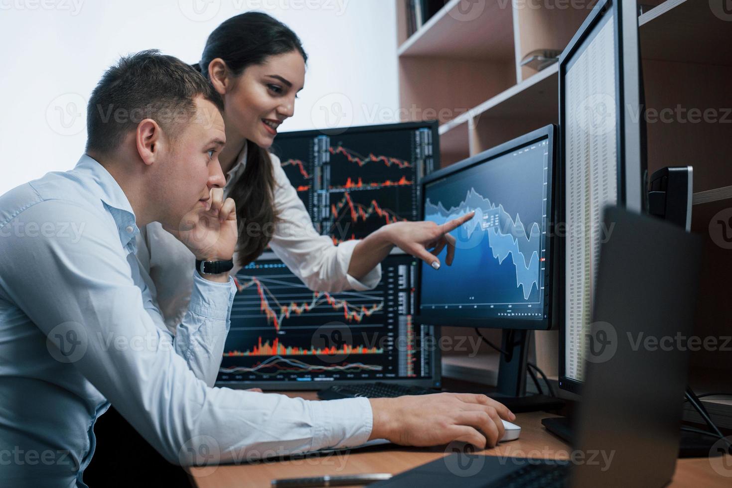 Girl is smiling, guy talks using the phone. Team of stockbrokers are having a conversation in a office with multiple display screens photo