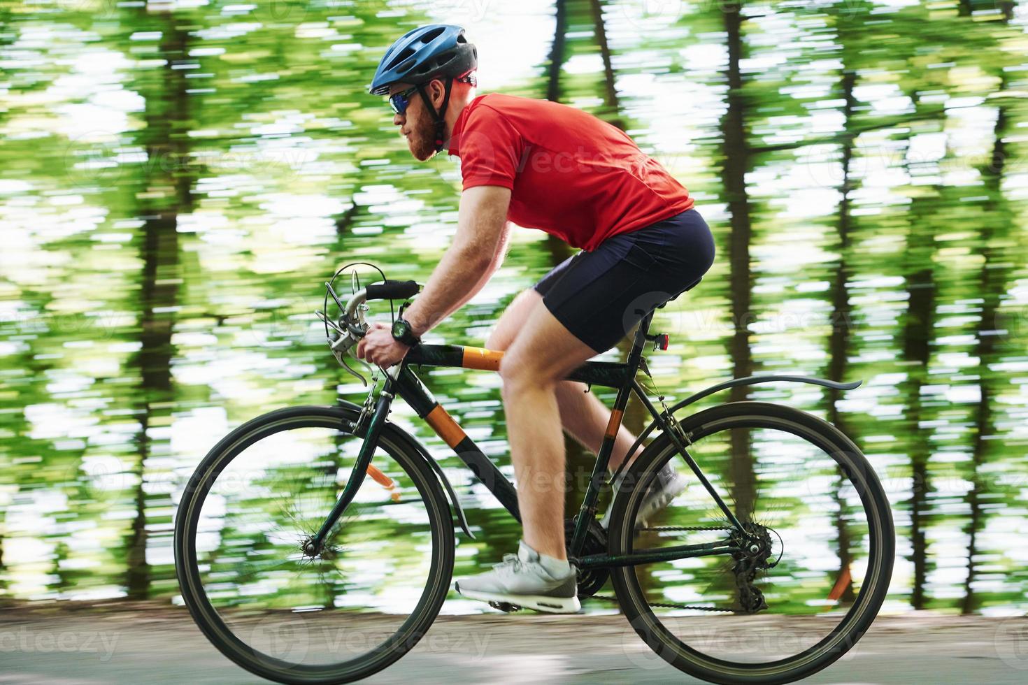 That's how healthy lifestyle looks like. Cyclist on a bike is on the asphalt road in the forest at sunny day photo