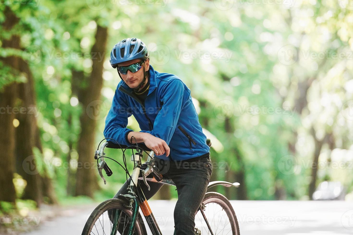 apoyado en la bicicleta. ciclista está en la carretera asfaltada en el bosque en un día soleado foto