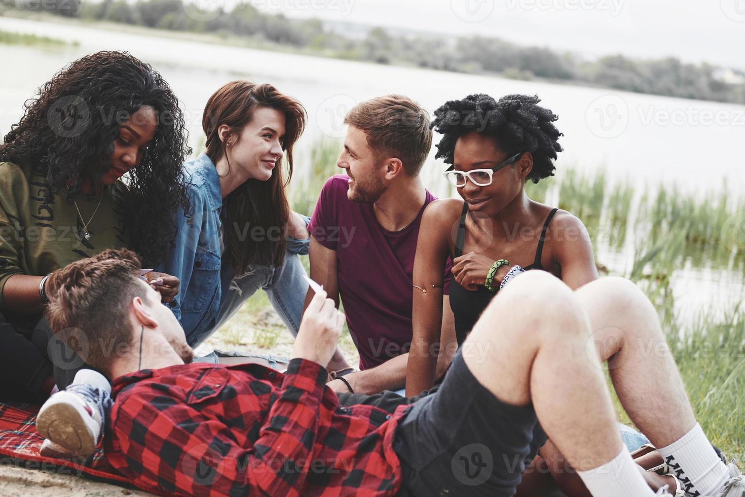 On red colored blanket. Group of people have picnic on the beach. Friends have fun at weekend time photo