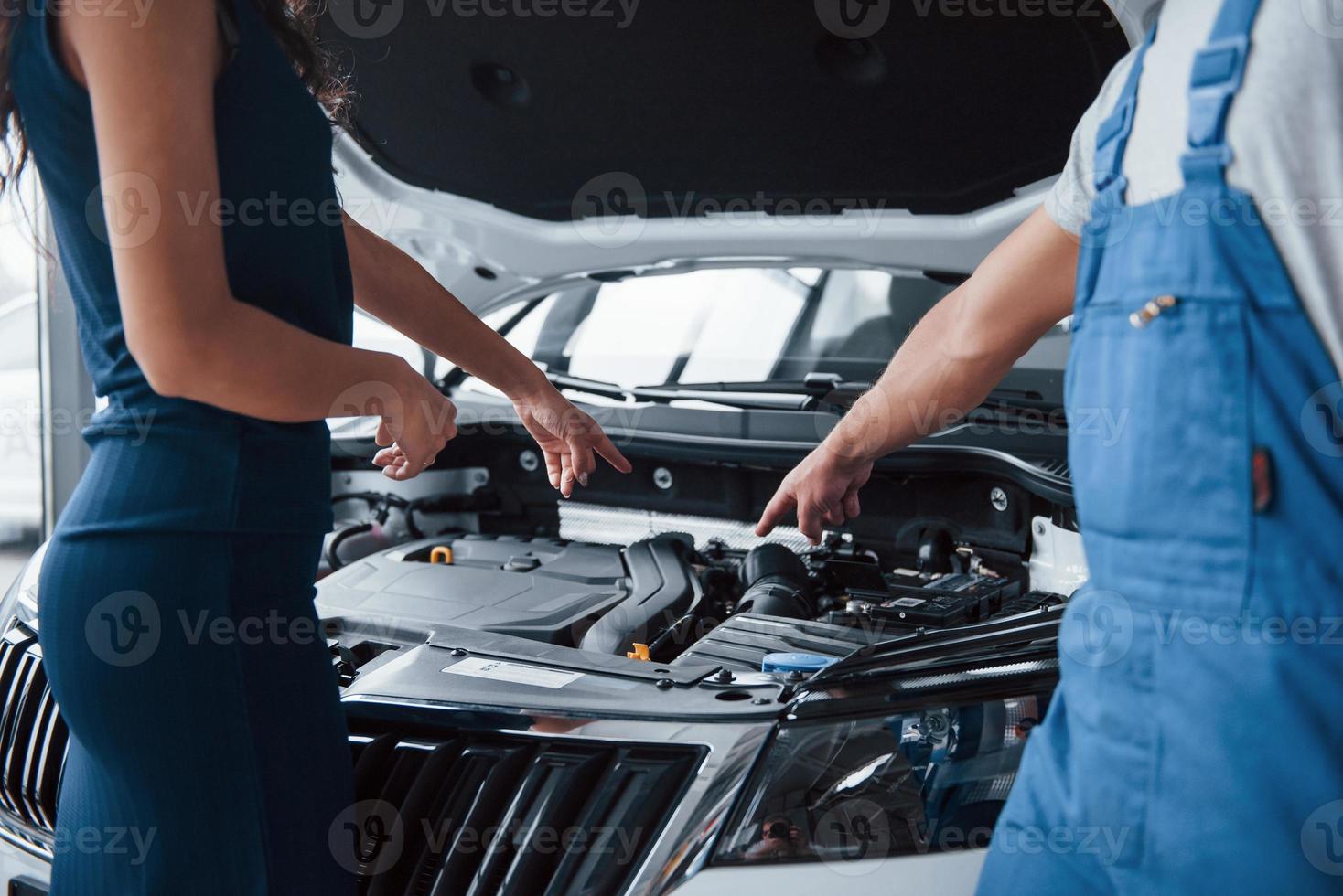 Supongo que tu problema en esa parte. mujer en el salón de autos con un empleado en uniforme azul que lleva su auto reparado de vuelta foto