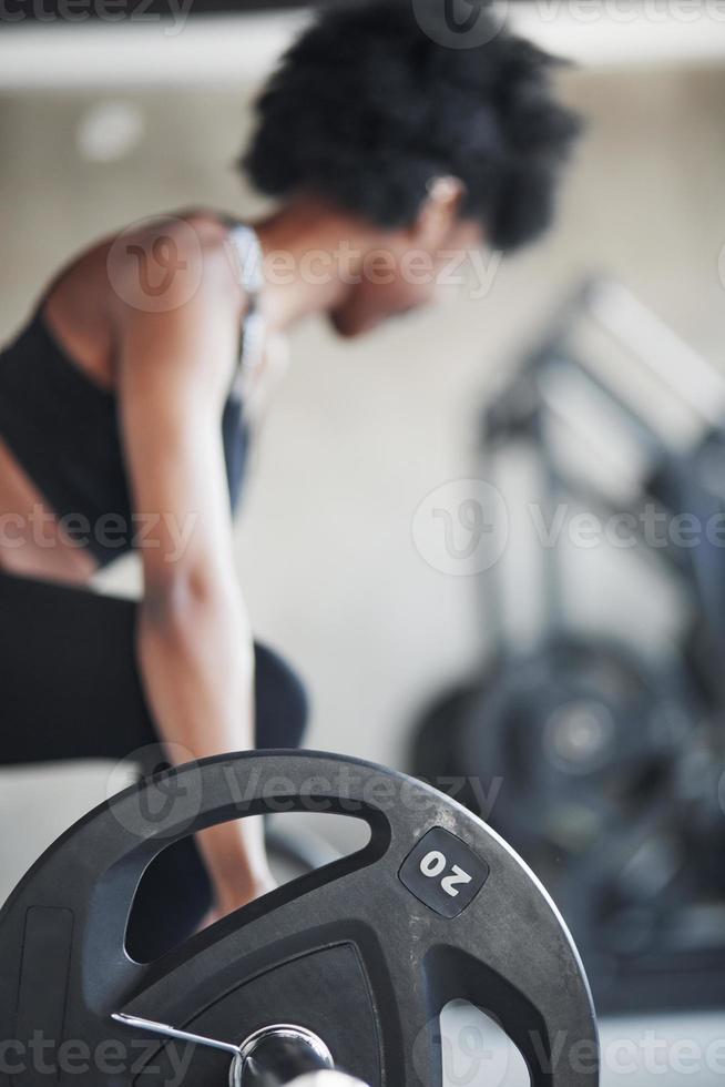 Hard working. African american woman with curly hair and in sportive clothes have fitness day in the gym photo