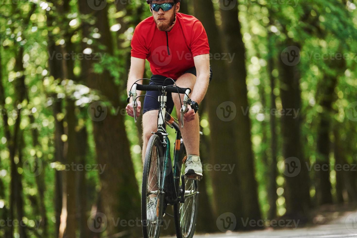 Nice background. Cyclist on a bike is on the asphalt road in the forest at sunny day photo