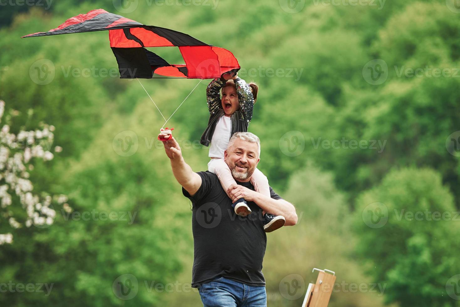 Enjoy the moment. Running with red kite. Child sitting on the man's shoulders. Having fun photo