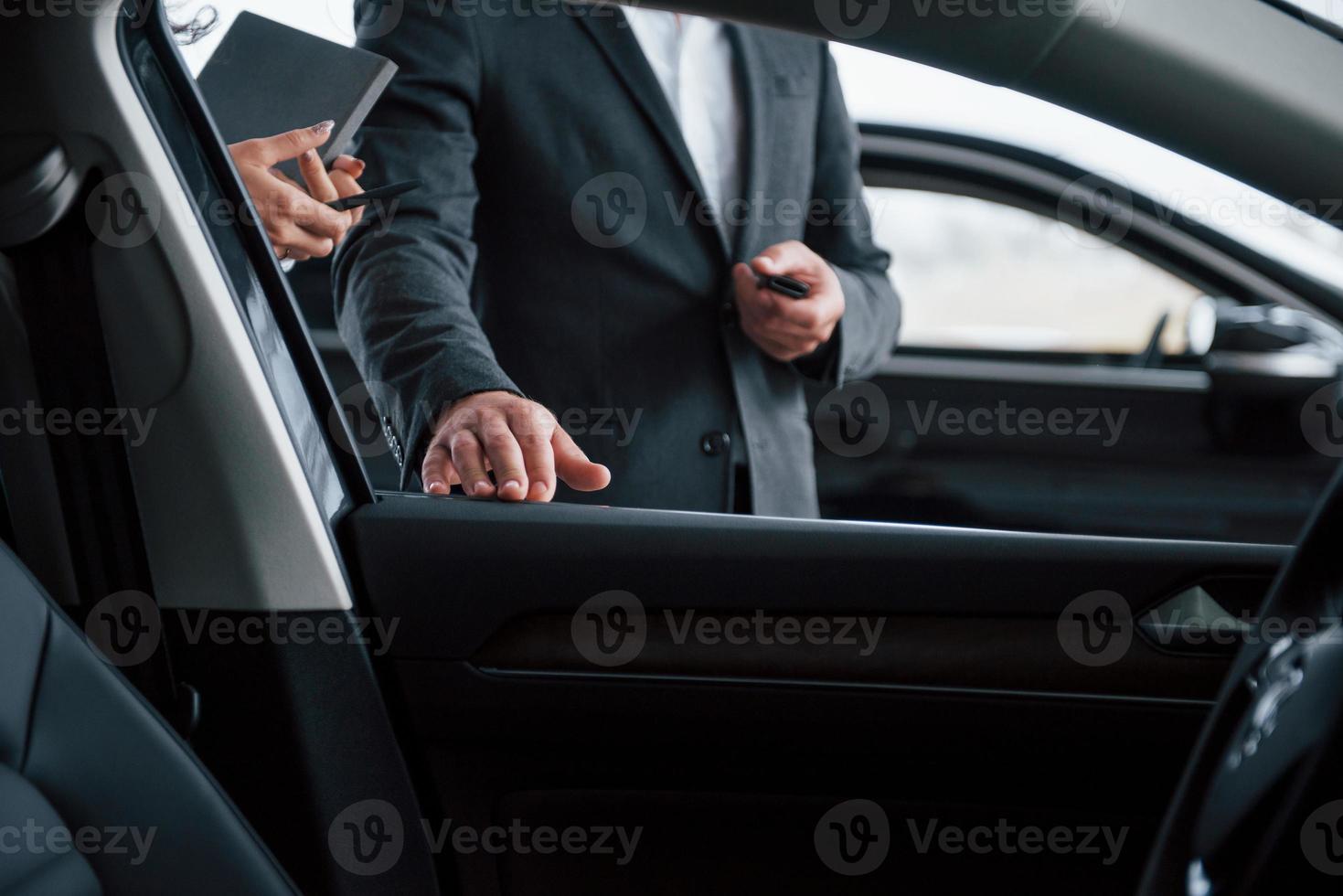 Photo from the inside of vehicle. Female customer and modern stylish bearded businessman in the automobile saloon