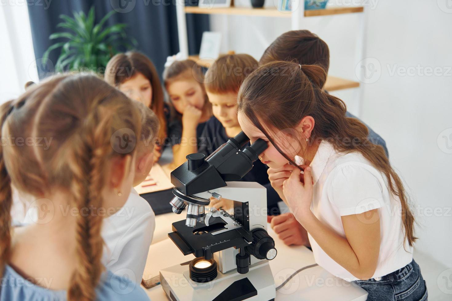 chica mirando al microscopio. grupo de niños estudiantes en clase en la escuela con el maestro foto