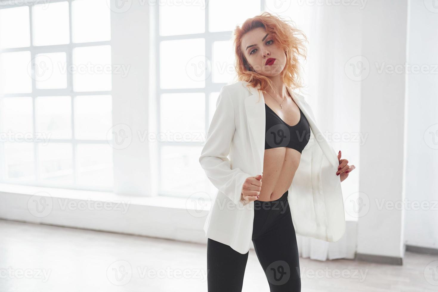 Feels the passion. Attractive redhead woman posing in the spacey room near the window photo