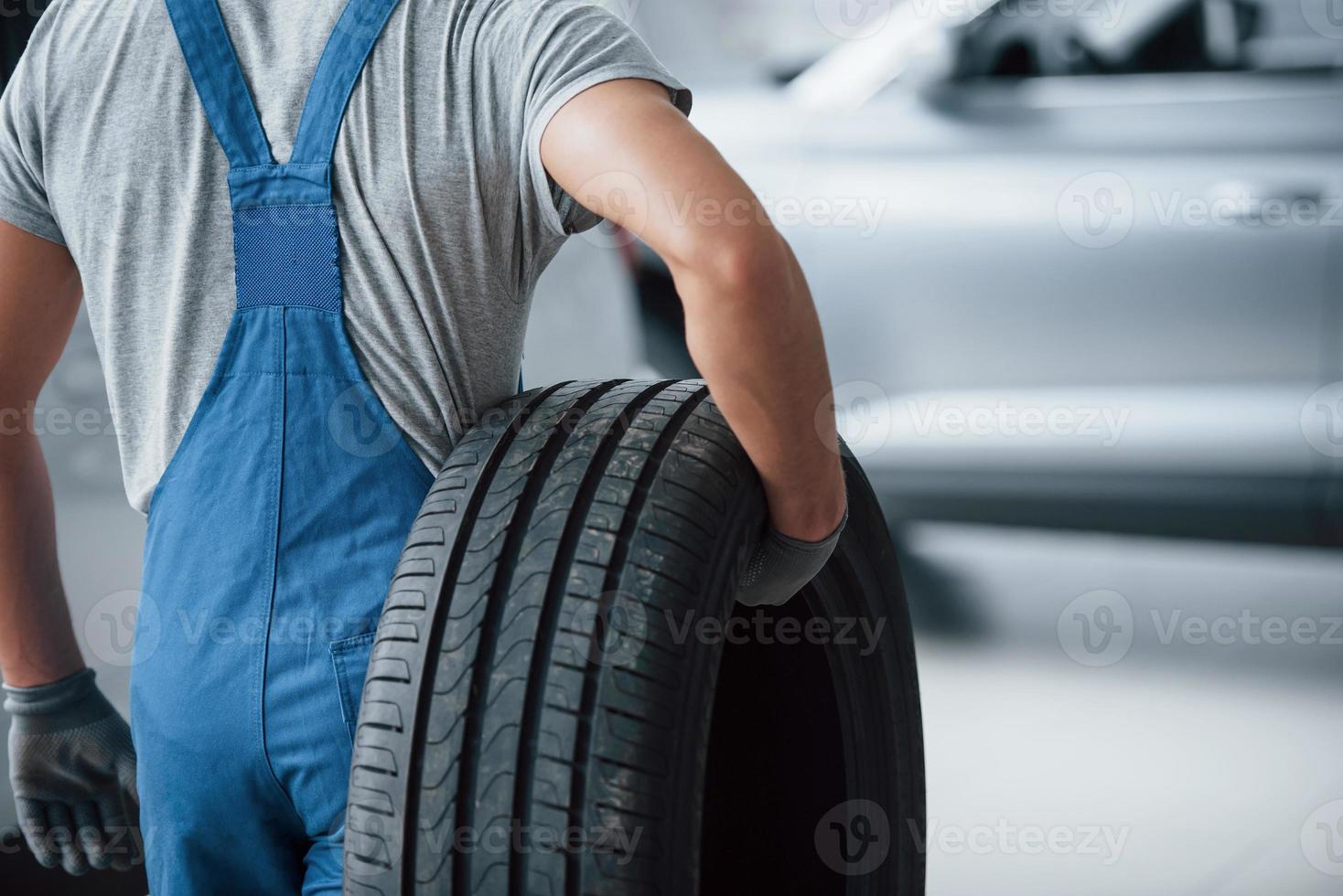 Repair concept. Mechanic holding a tire at the repair garage. Replacement of winter and summer tires photo