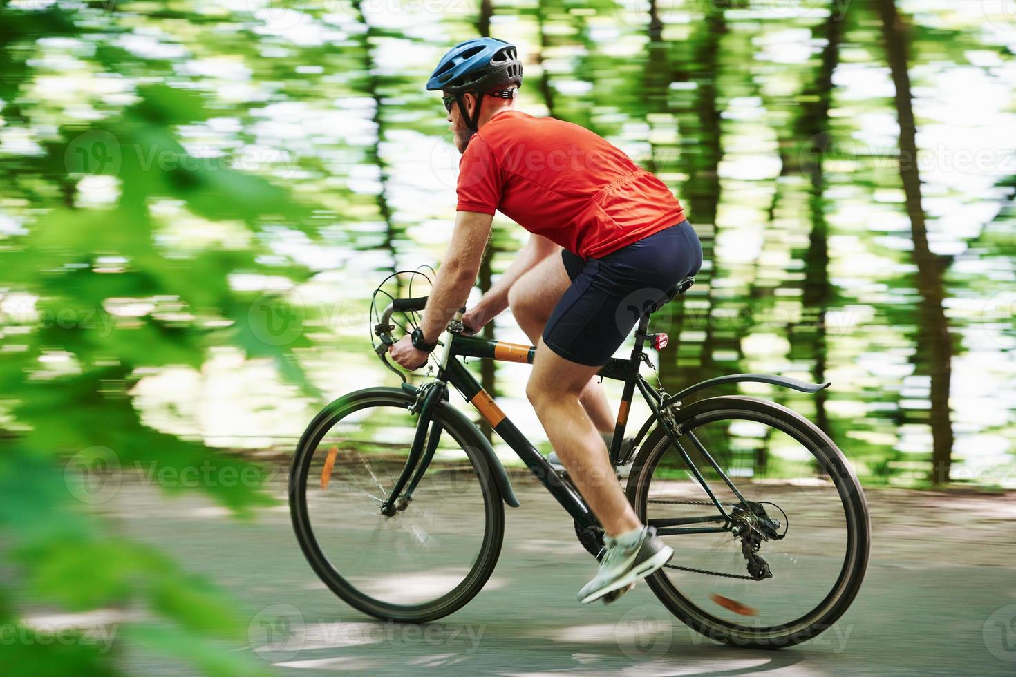 Rural scene. Cyclist on a bike is on the asphalt road in the forest at sunny day photo