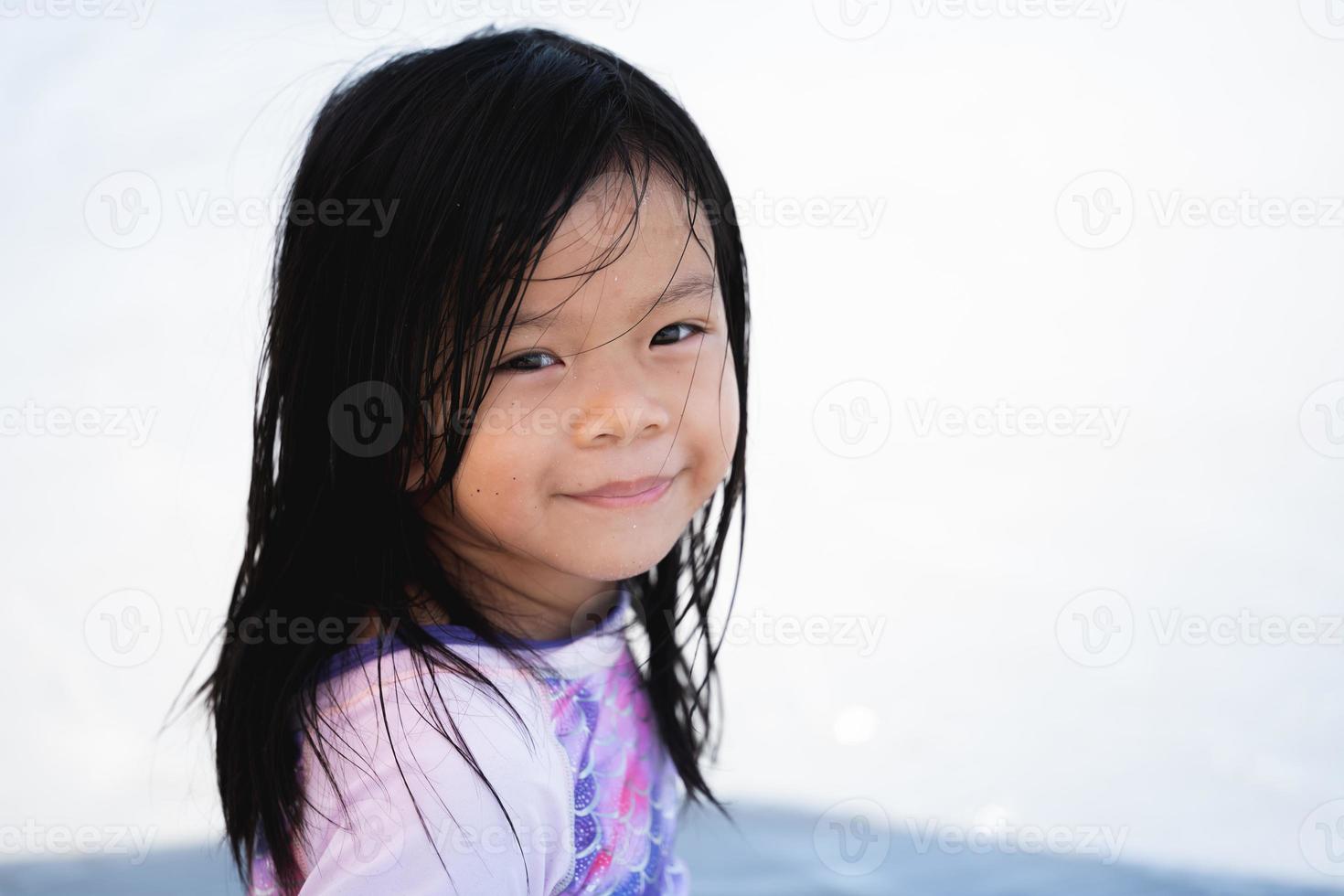 Portrait image child 5 years old. Positive smiling little girl looking at camera. Kid sitting on beach, preschool pretty children with beautiful happy face posing alone at sea, cheerful baby headshot. photo