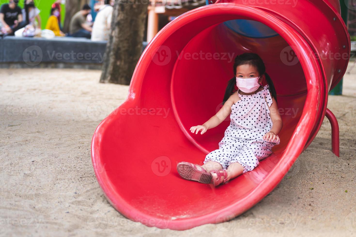 Portrait image child 5-6 years old. Asian girl playing slider at playground. Kid have fun with leisure activities. Play is good learning for baby. Children wear face mask prevent PM2.5 dust and virus. photo