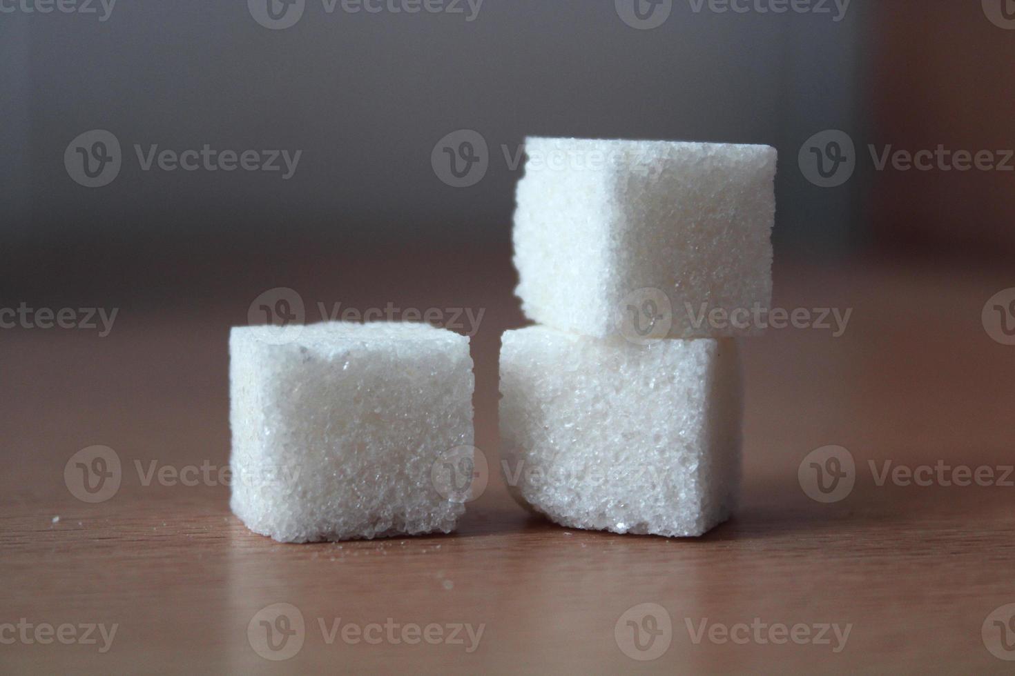 Closeup of three white sugar cubes on blurred background, horizontal photo. Culinary product for cooking, refined sweet eating, tea and coffee supplement photo