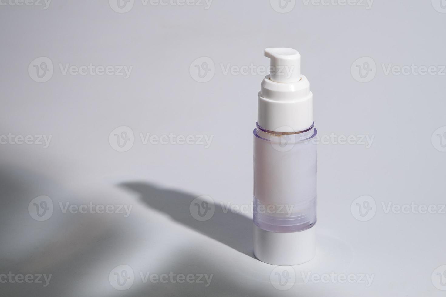 paquete cosmético y de cuidado de la piel en una botella de vidrio sobre fondo blanco con sombras duras o duras y luz solar de la rama del árbol de hojas cayendo sobre la pared. diseño de productos de belleza moderno y minimalista. foto