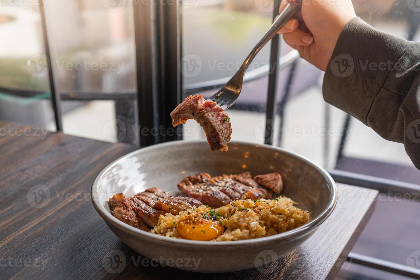 arroz frito con ajo y grasa de ternera con bistec de ternera y cubierta con yema de huevo en escabeche en un bol sobre una mesa de madera. carnes a la parrilla foto