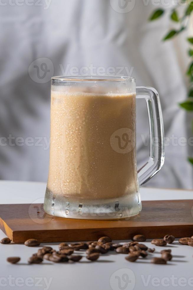 Cold coffee drink glass with ice and cream milk on old white table in abstract silhouette shadow white background of natural leaves tree branch falling on wall. latte and cappuccino refreshment. photo