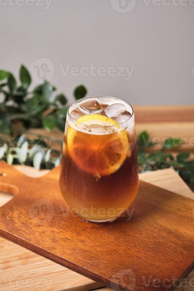 cold iced black brew coffee mixed lemon juice and lemon slices in a glass with pieces of ice on a wooden table, natural light, fresh summer drink in the morning photo