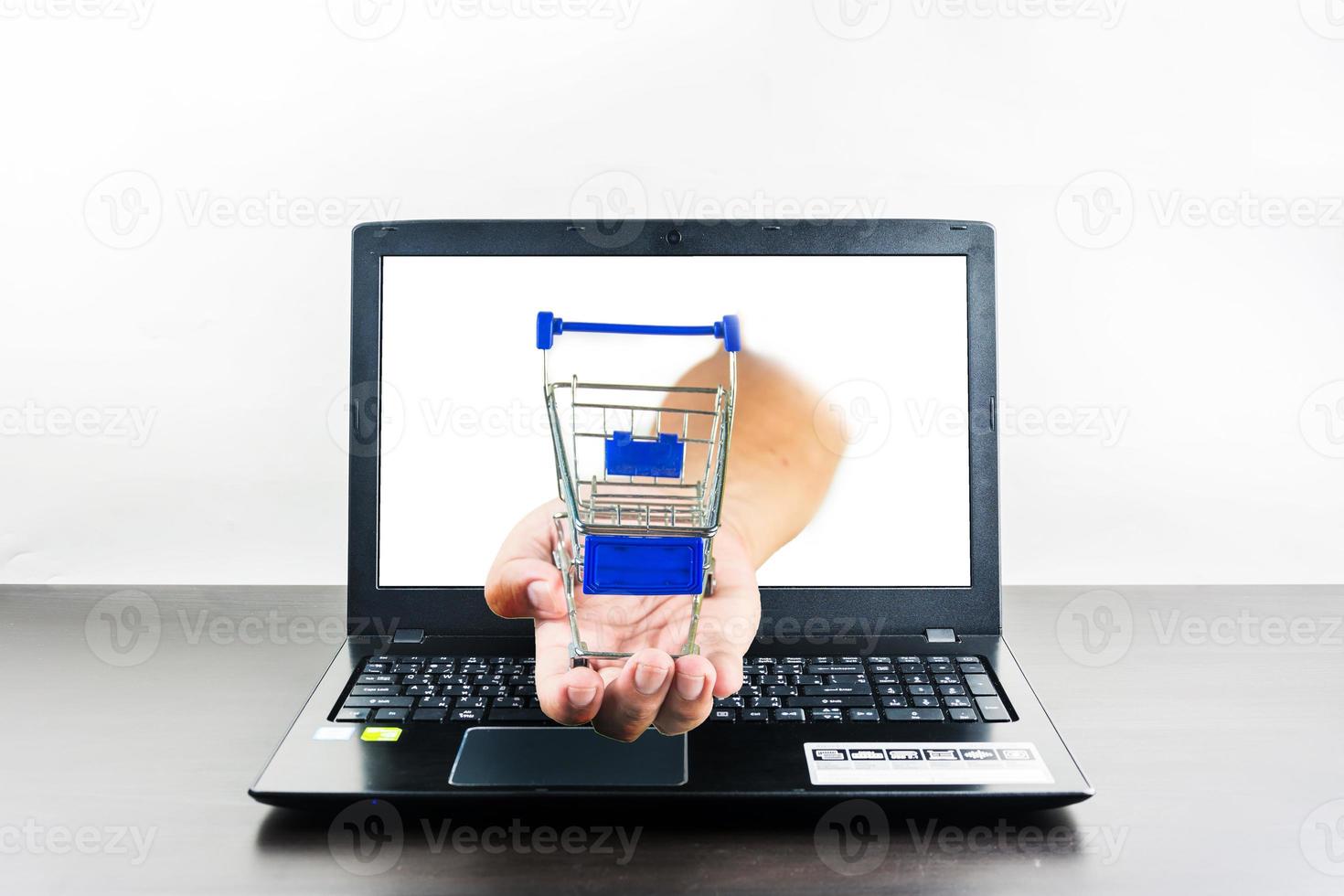 carro de la compra en la mano con la pantalla en blanco de la computadora portátil en la mesa de madera foto