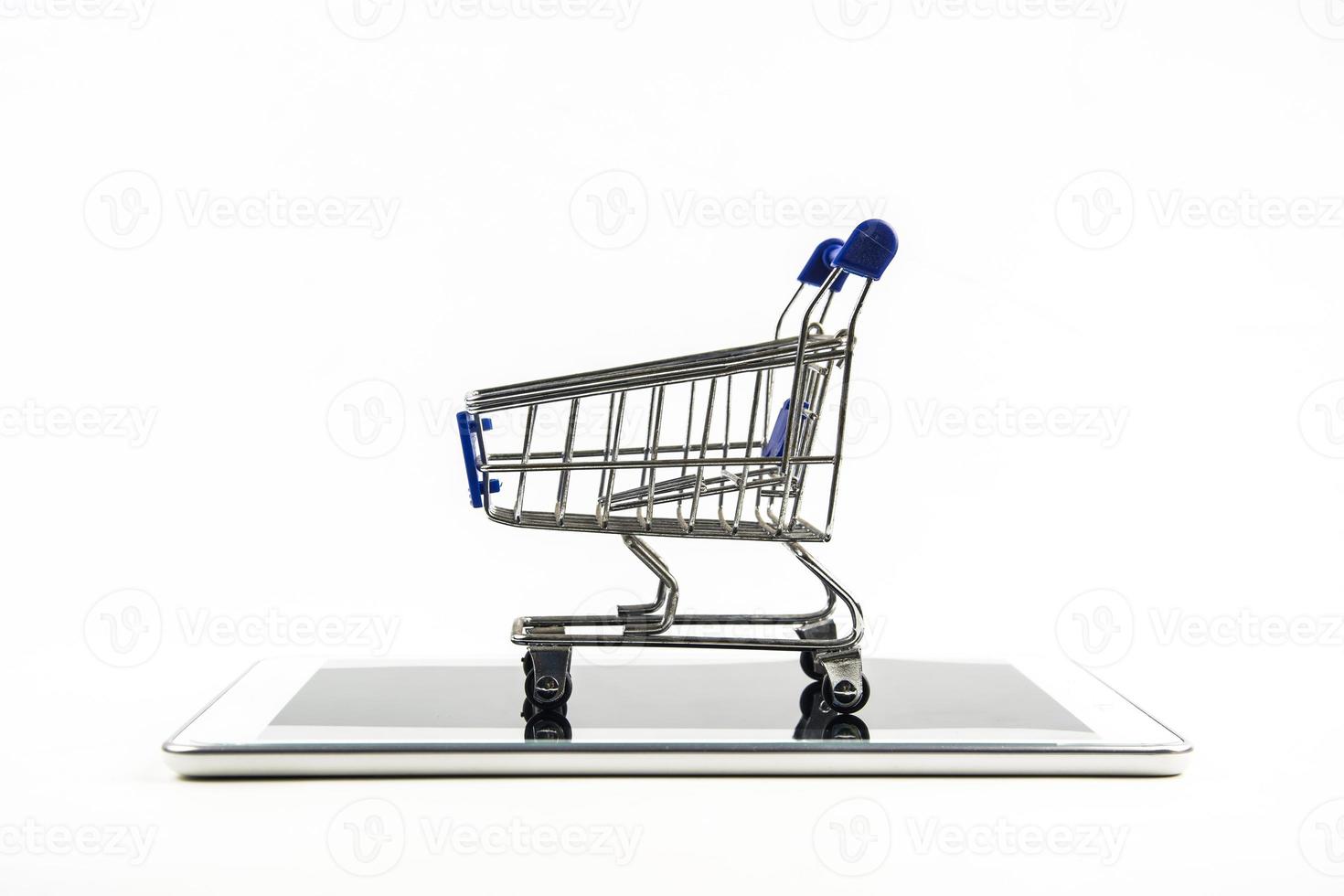 carrito de compras con tableta en backgrond blanco, significa comprar en línea foto