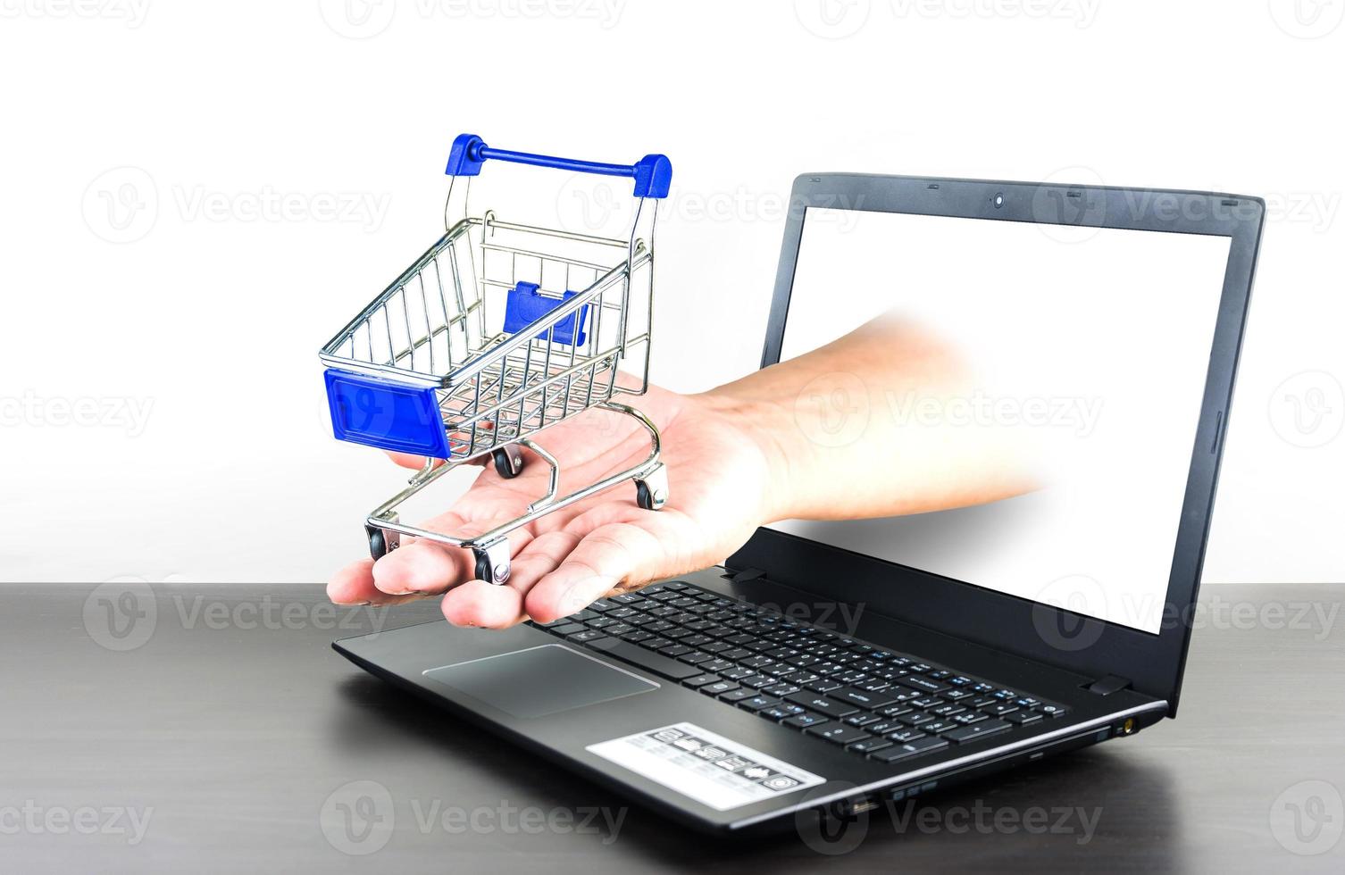 shopping cart in hand with Computer notebook blank screen on wood table photo