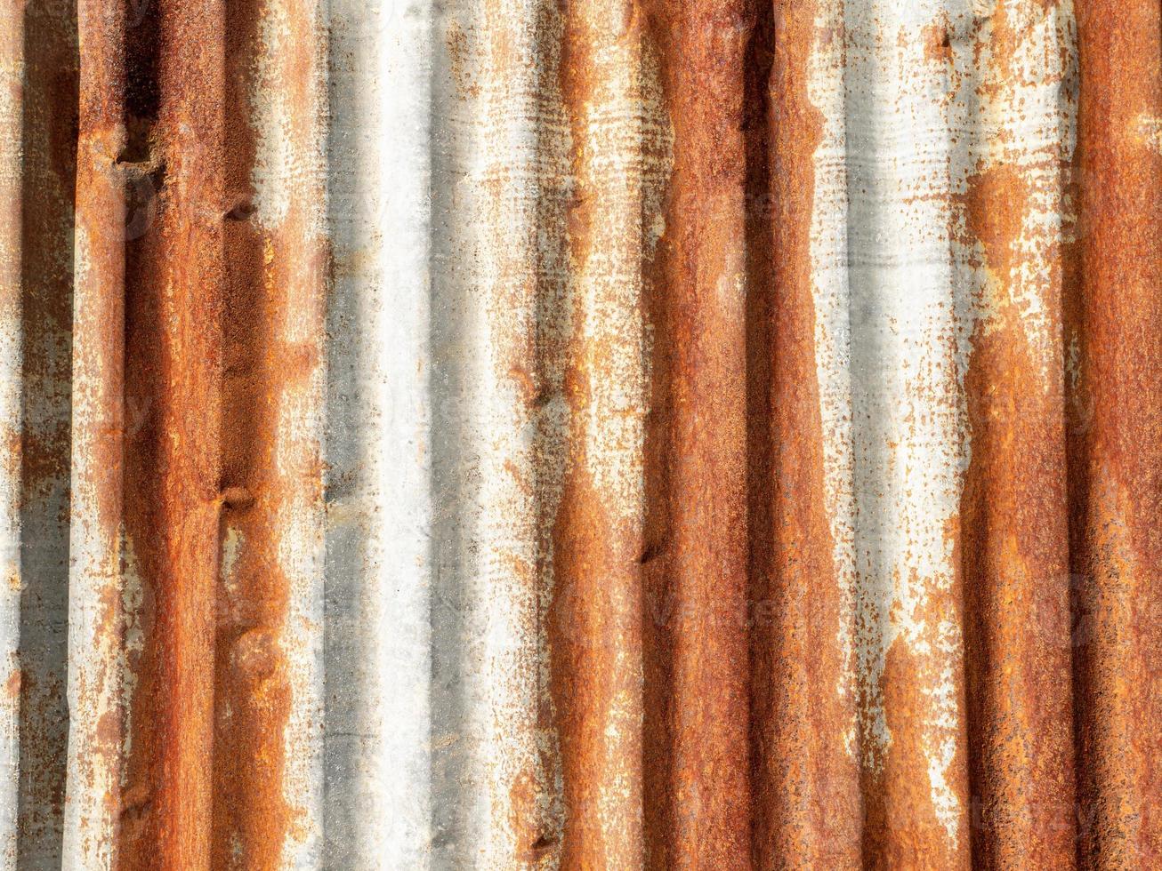 Old galvanized walls rusted and decayed due to sun exposure and rain, causing the surface to be rough and discolored. photo
