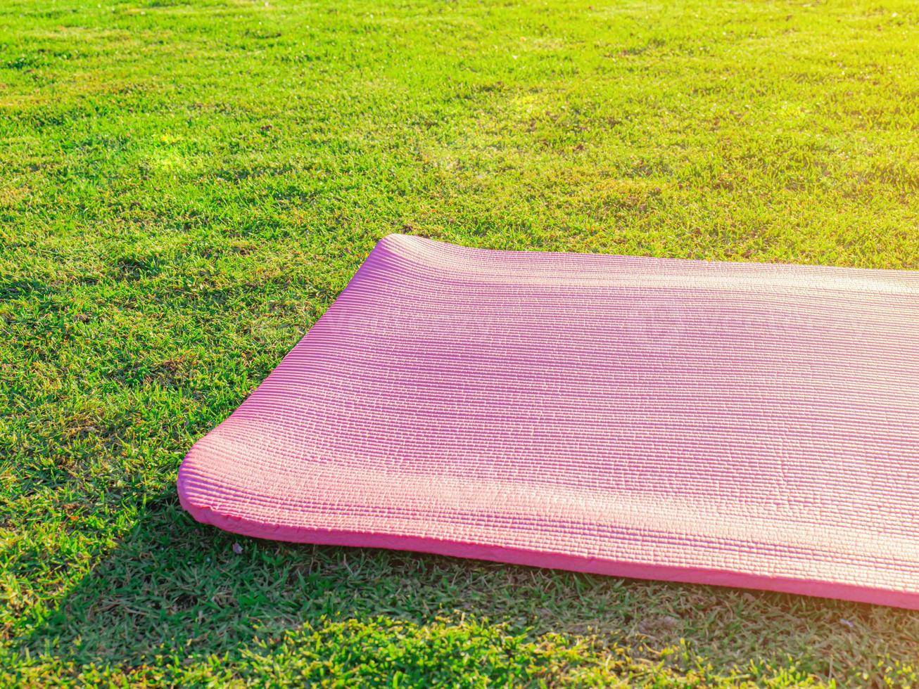 Pink yoga mat laid on green grass In the park in the evening there was a soft sunlight. The warm light tones are suitable for yoga exercises. photo