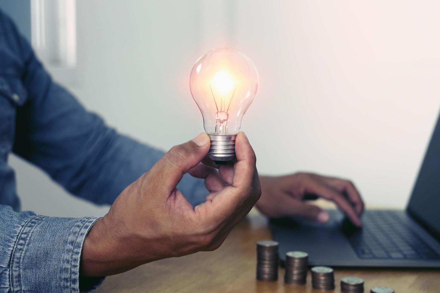 mano que sostiene la bombilla con el uso de la computadora portátil en la oficina. concepto de energía de ahorro de energía foto