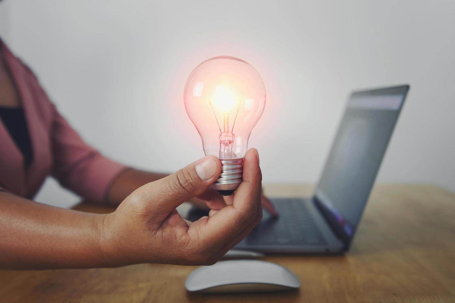 business woman hand holding light bulb with using laptop in office. concept saving energy power photo