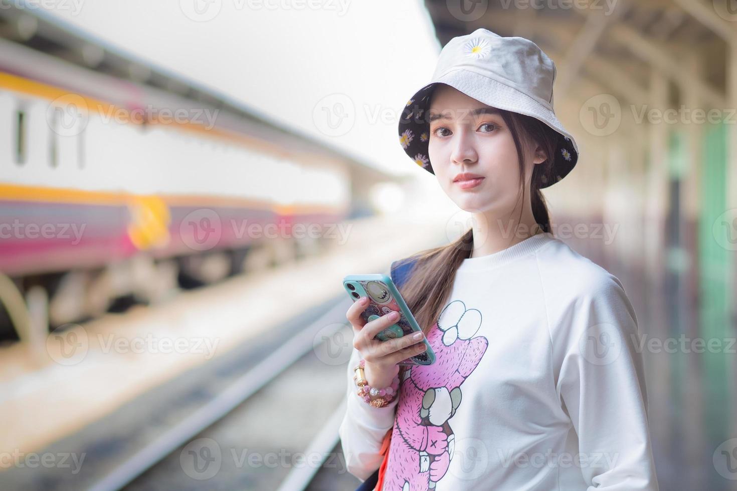 Asian beautiful  woman holding a bag and a smartphone in search of travel information. While waiting for the train at the platform. photo