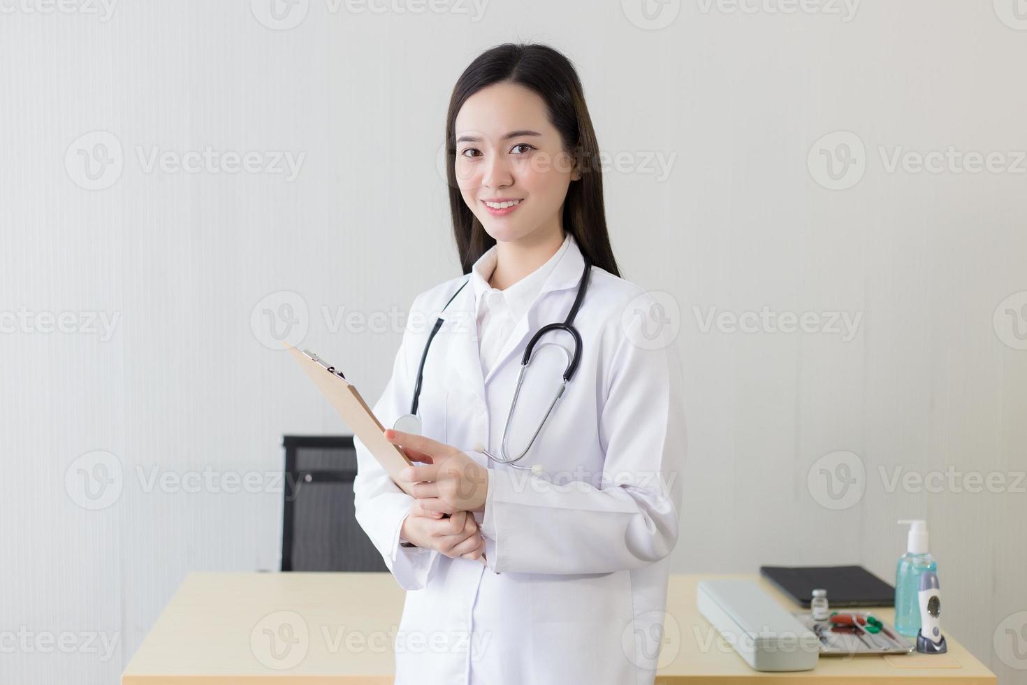 Asian woman doctor examine report document of patient to plan the next treatment. She look at the clipboard in her hand while working at hospital. photo