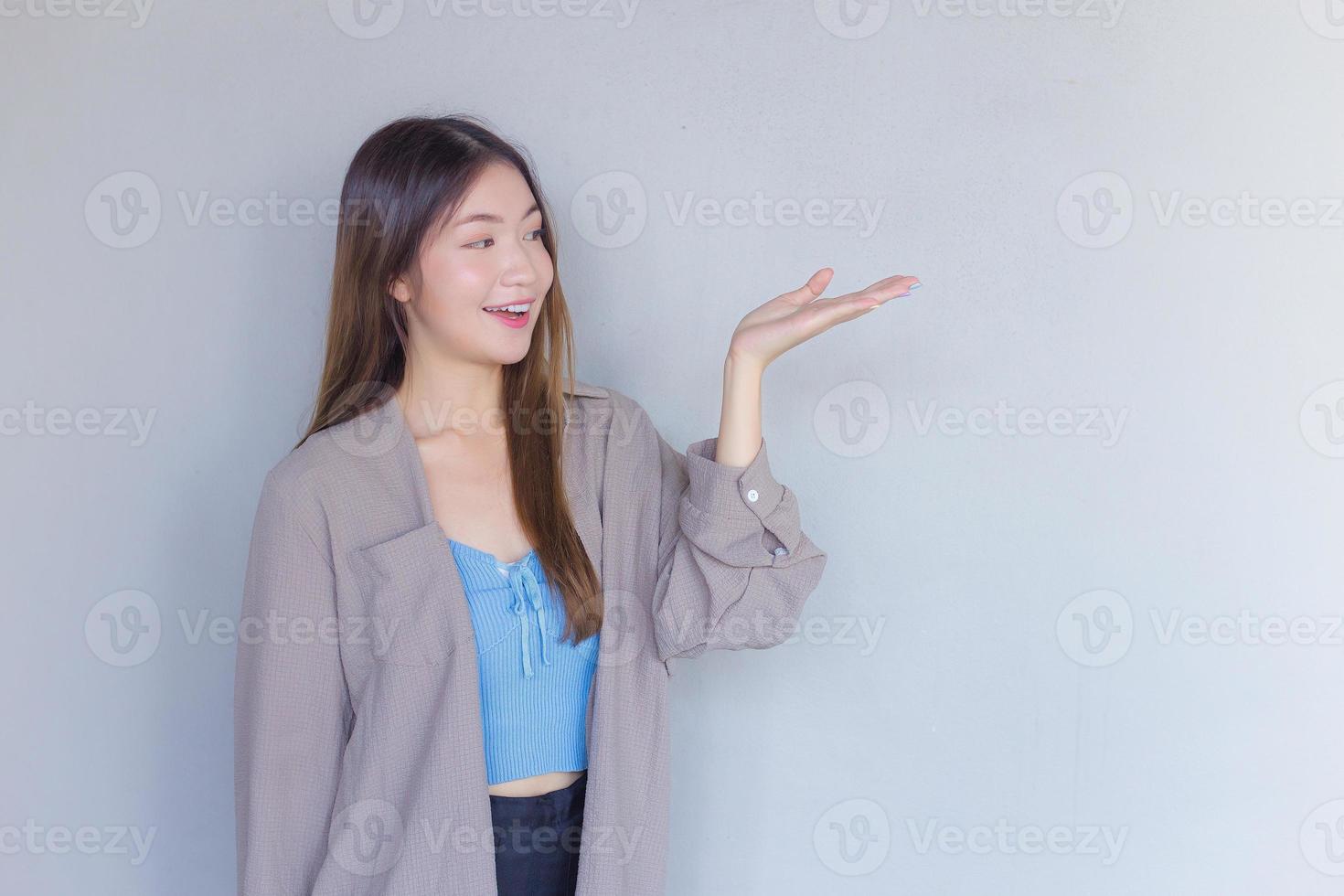 Beautiful young Asian woman long brown hair in a blue shirt is acting hand shows as presenting something on the background. photo