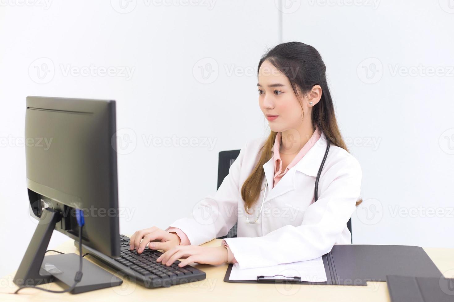 Asian beautiful woman doctor is typing on a keyboard to save information on the computer. New normal and healthcare concept. photo