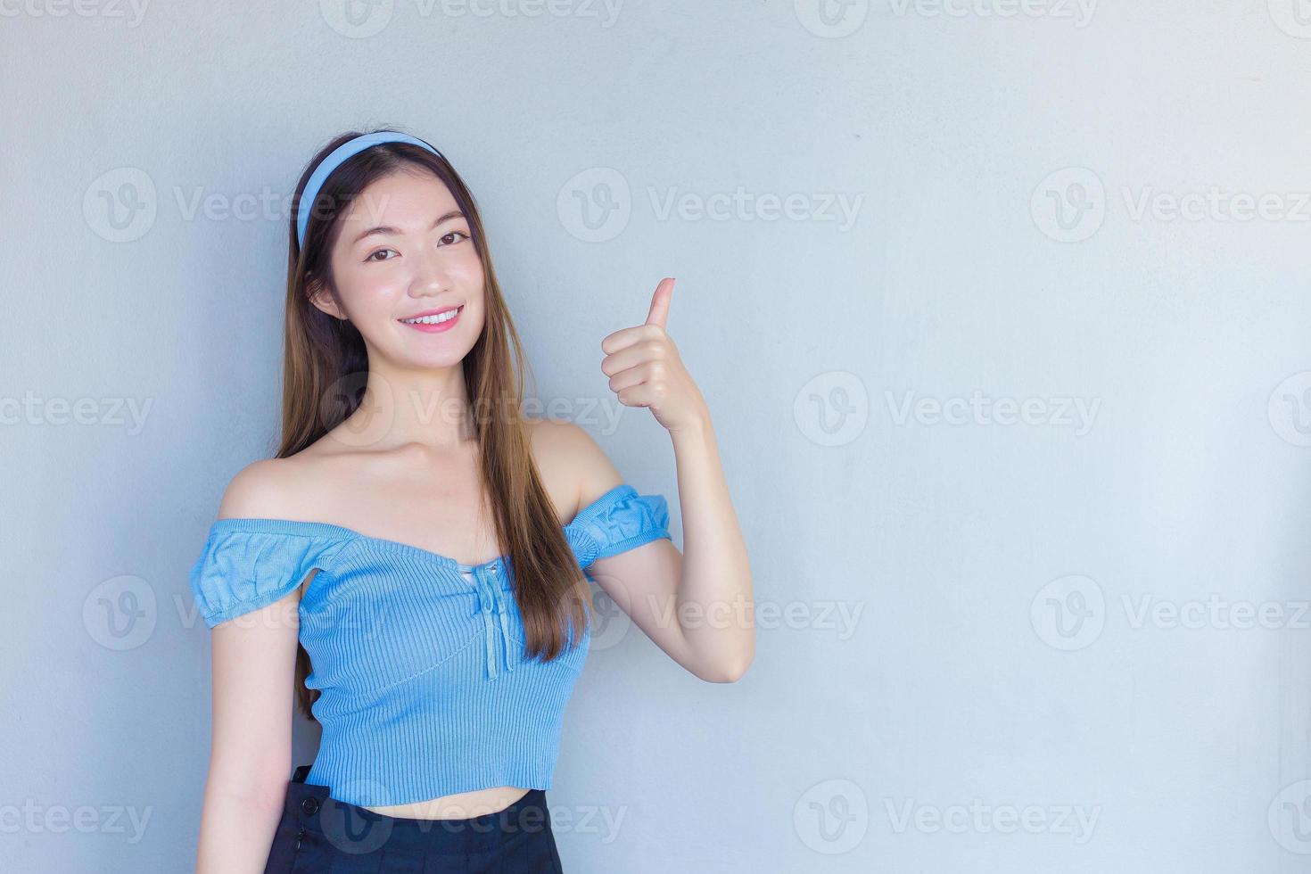 Young beautiful Asian woman is acting thumb up as a good symbol and another hand shows as presenting something on the background. photo