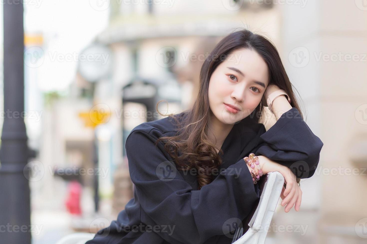 Portrait Asian beautiful woman in dark blue long sleeve shirt sits on chair in park outdoor. photo