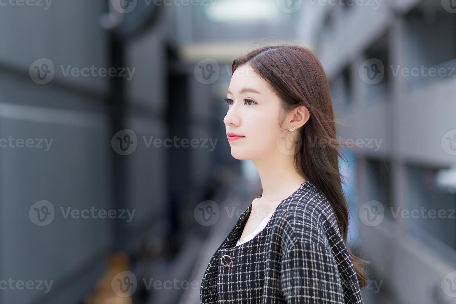 Portrait of a beautiful, long-haired Asian woman side face in a black pattern coat with braces on teeth standing and smiling outdoors in the city. photo