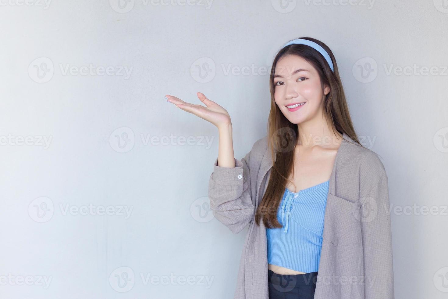 Beautiful young Asian female long brown hair in a blue shirt is acting hand shows as presenting something on the background. photo